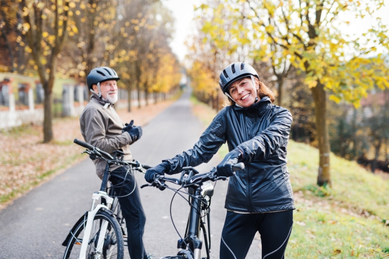 A smiling couple in helmets with their bikes on a tree-lined autumn path
