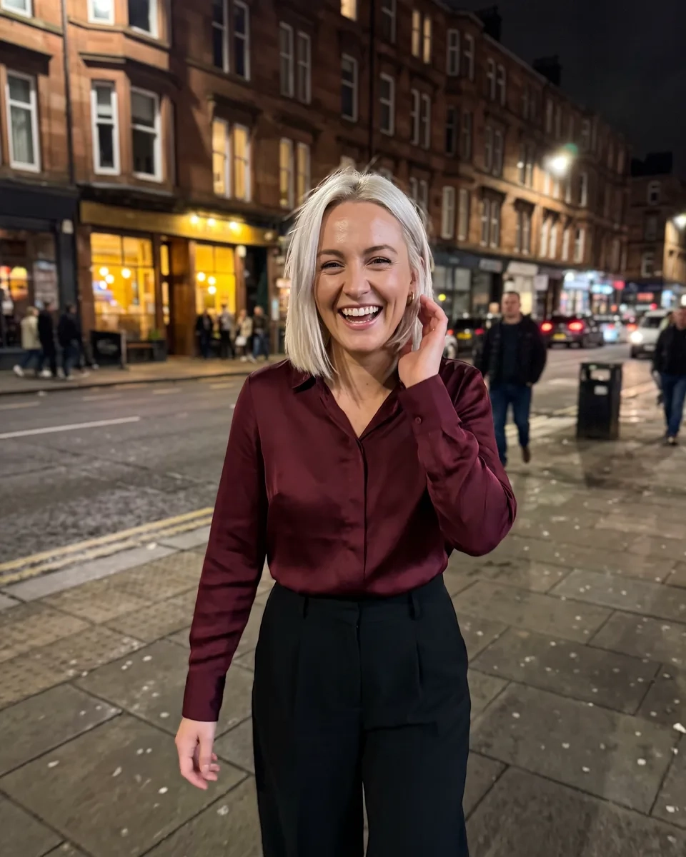 A woman with a sleek platinum blonde bob in a burgundy satin blouse walks laughing along a lit street of red sandstone tenements in Finnieston, Glasgow, at night (AI-generated image)