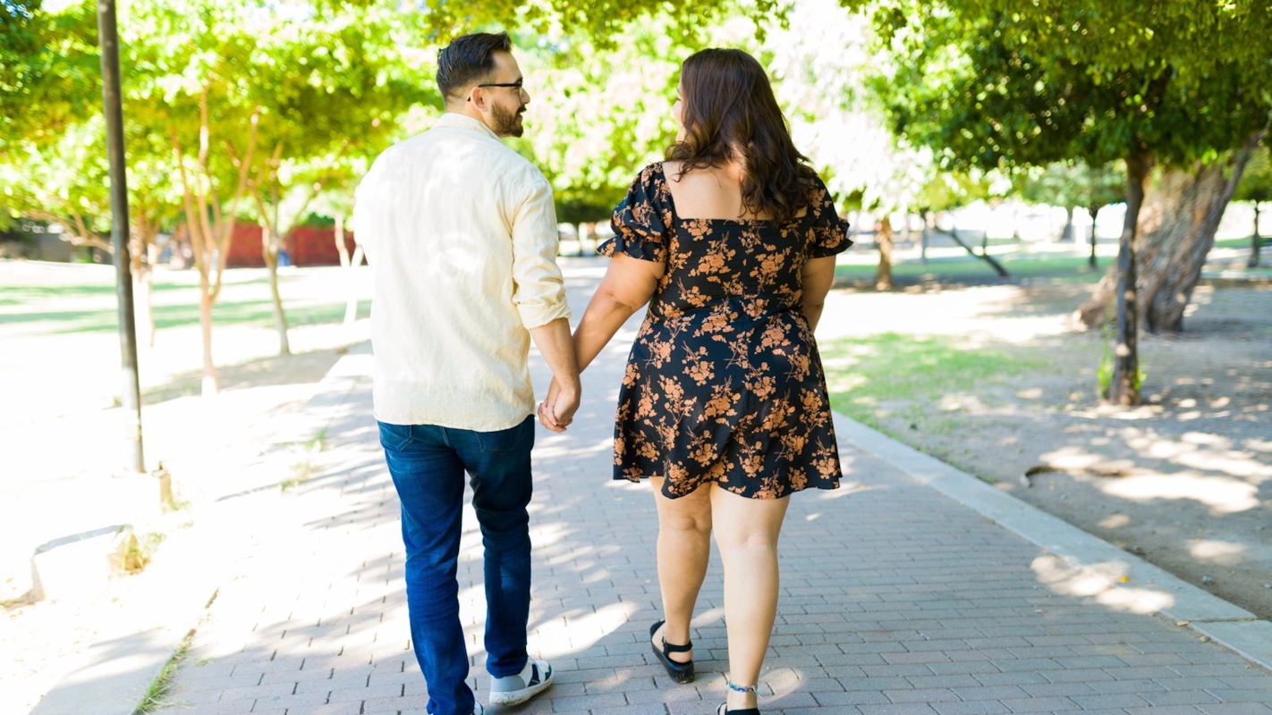 A couple walking hand in hand through a sunny park