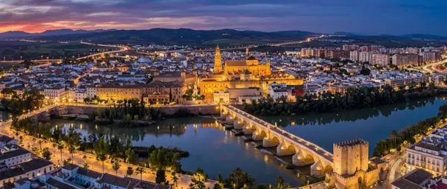 Puente romano de Córdoba y la Mezquita-Catedral iluminados al atardecer junto al Guadalquivir