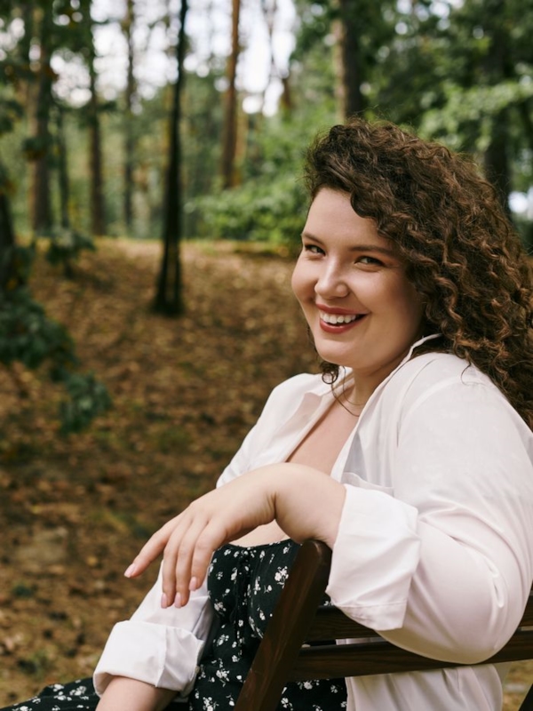 A curvy woman with curly hair smiling outdoors
