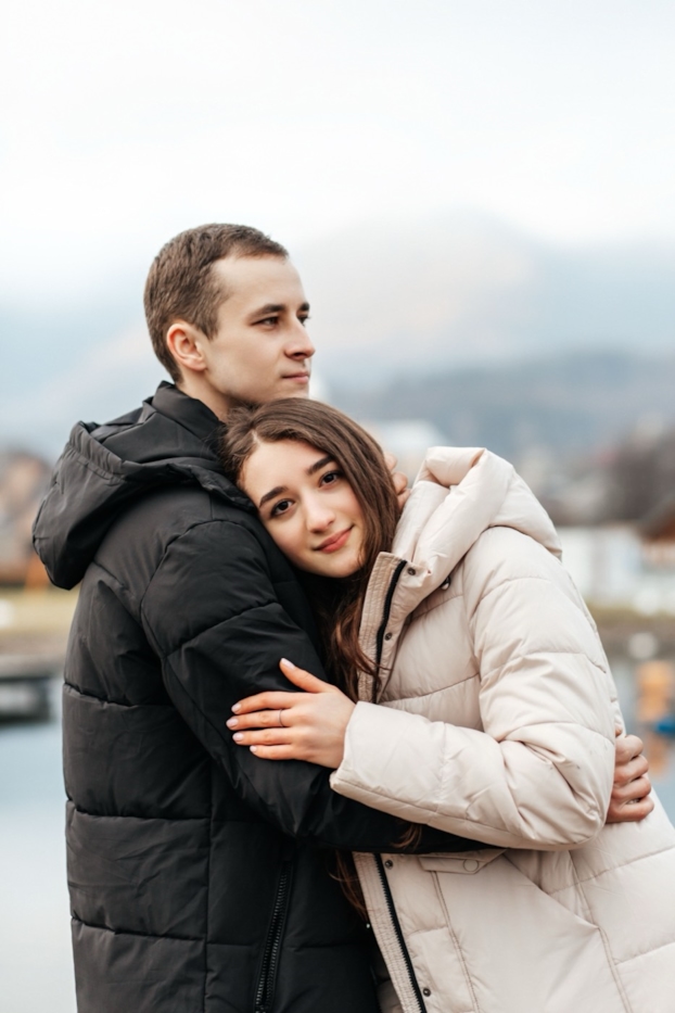 A couple in winter coats shares a close embrace outdoors