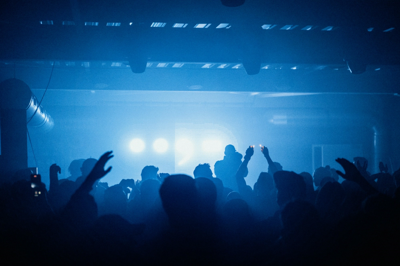A crowd with their hands up under blue lights at a club night