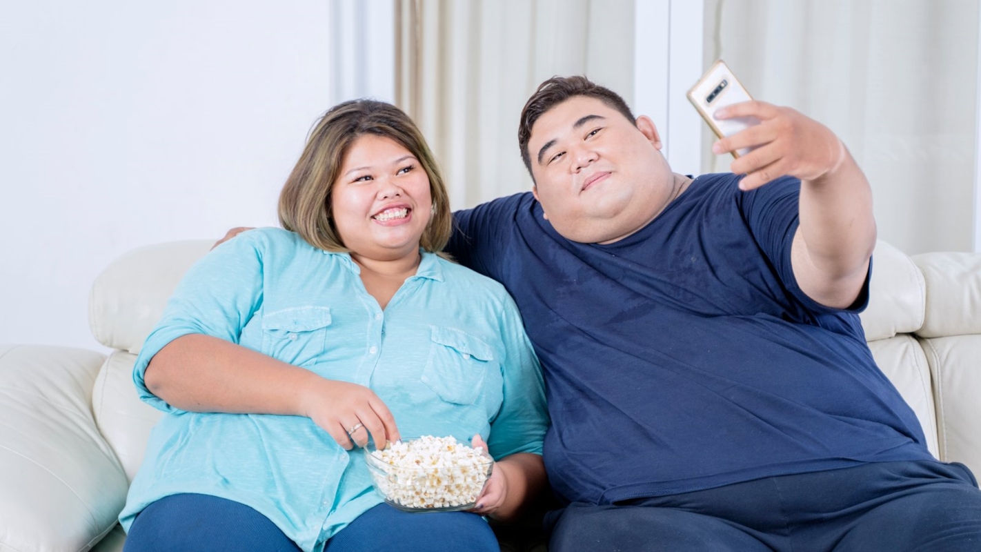 A couple relaxing on the sofa together, taking a playful selfie with popcorn