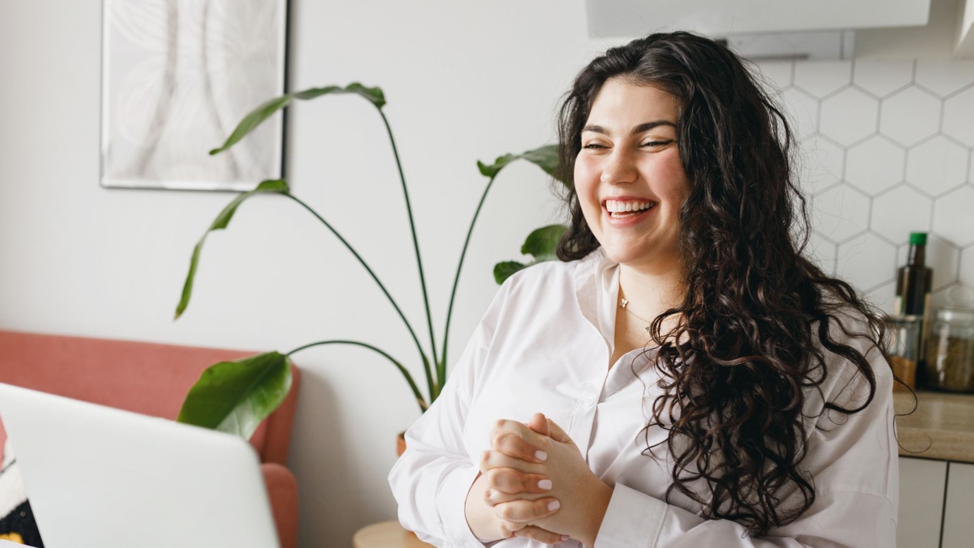 A woman laughing while sitting at her laptop in a bright home office