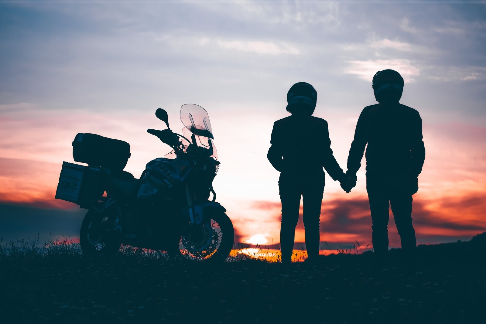 Silhouette of a couple holding hands beside a touring motorcycle at sunset